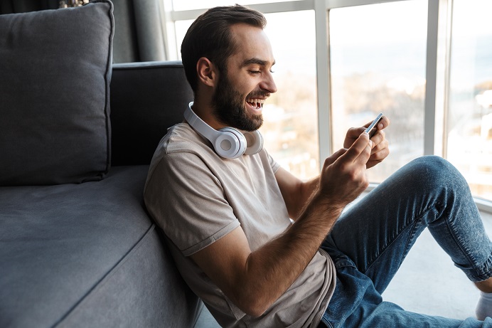 middle-aged man with beard using PlayPhone games app while sitting on floor